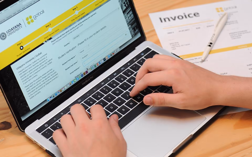 Student applying online in myUNUD for a semester in Bali, with a GoBali invoice next to the laptop