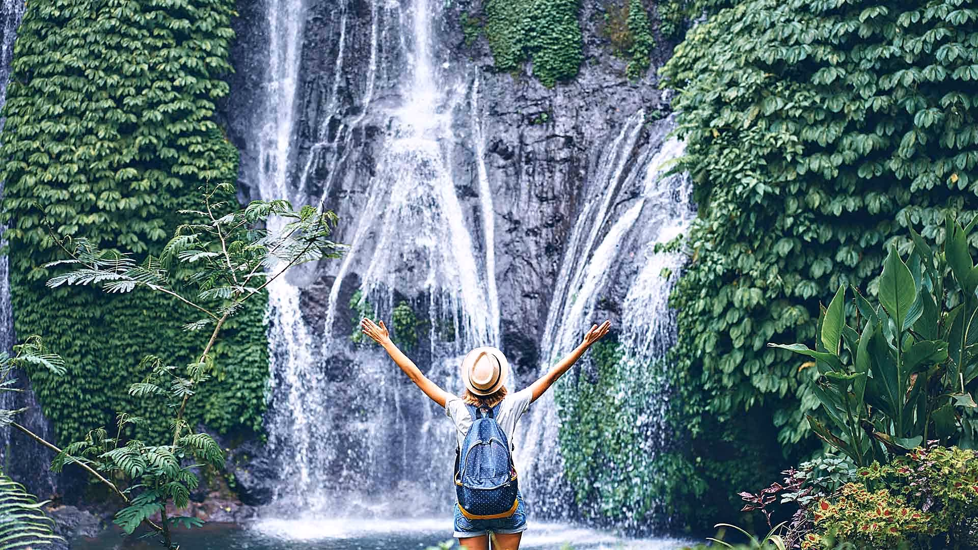 Student with arms raised in front of a waterfall in Bali
